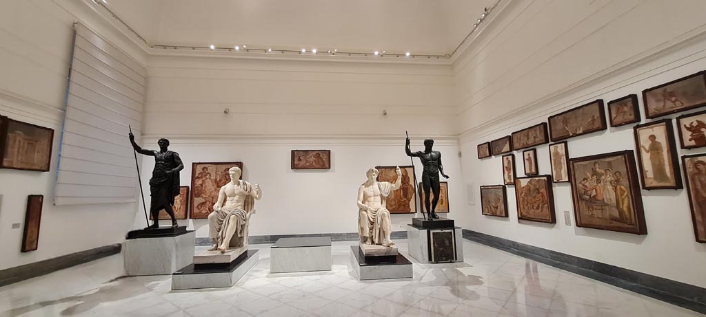 Herculaneum Augusteum. April 2023. 
Looking across gallery towards statues on display in “Campania Romana” gallery in Naples Archaeological Museum.  
(Note: the central statue of Titus is missing, see below for a photo including it).  Photo courtesy of Giuseppe Ciaramella.

