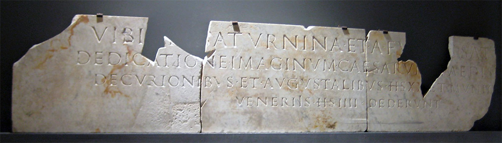 Herculaneum, Sacred Area terrace. 2017. Temple of Venus. Dedicatory inscription of the busts of Titus and Domitian.
According to the Epigraphic Database Roma this reads:
Vibi[d]i[a] Saturnina et A(ulus) Fu[riu]s Satu[rninus]
dedicatione imaginum Caesarum [e]t aedis V[eneris]
decurionibus et Augustalibus ((sestertios)) XX et munic[ipibus ((sestertios)) - - - et]
Veneriìs ((sestertios)) IIII dederunt.      [ EDR103045]

According to Alison Cooley:
It was not just freedmen who could achieve such standing in the community. One of the most recently excavated parts of Herculaneum provides fresh evidence for the role that a freedwoman might play in civic life. Down above the harbourfront, a temple has recently been uncovered, which was dedicated to Venus. Originally constructed in the second century B.C., the temple was modified in the Augustan period, and then repaired during the early Flavian period, just a few years before being destroyed in the eruption. This temple has two monumental building-inscriptions which tell us the interesting background to this last building-phase. These inscriptions were found
shattered into pieces on the beach-front, hurled there, no doubt, by the pyroclastic surges.
The first of these inscriptions states:
‘Vibidia Saturnina and Aulus Furius Saturninus, at the dedication of the portrait-busts of the Caesars [Titus and Domitian] and of the temple of Venus, gave to the town councillors and Augustales 20 sesterces each and to the townsfolk [8?] sesterces, and to the worshippers of Venus 4 sesterces.”
See Cooley, A., 2013. Social climbers at Herculaneum. Omnibus (London), Vol.65 . pp. 19-21.
