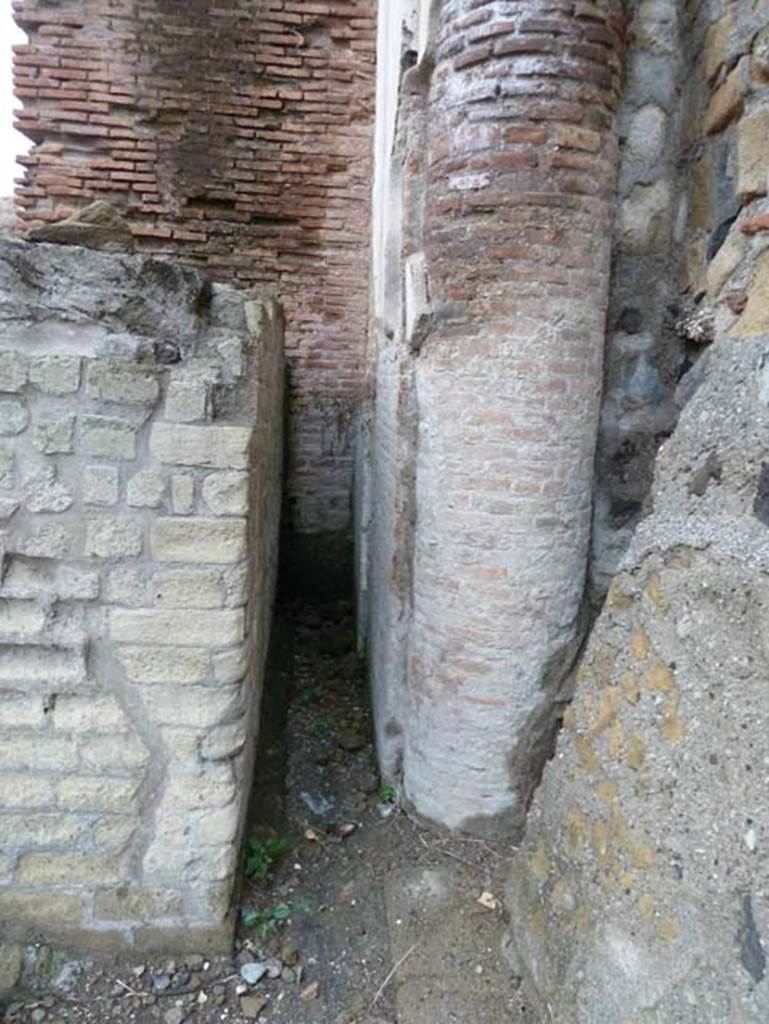 Herculaneum, September 2015. Looking west towards statue base, on left, and column at the rear of it.
The masonry wall at the rear is part of the four-sided arch. 
