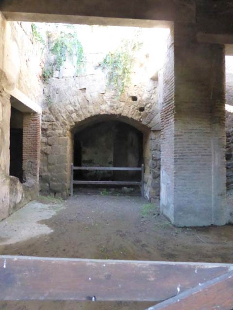 II.2 Herculaneum, September 2015. Looking west through doorway from west portico.
According to Pagano – “Turning to the other side of the garden you pass into another portico that also had its garden in the middle. 
This can be said to be the most preserved part of the excavation.
The walls are painted in black, with panels surmounted by white with architectural designs of good taste and lightness, the pillar facing the door, painted in red, fluted, and with beautiful frieze above coloured stuccos was admirable. The artistic effect would have been prodigious, for the prominence that produced in their freshness the columns of white stucco against the black background of the walls around. The floor in black and white, of the room not entirely discovered, towards the right side of the door. could still be observed. The most preserved part was the one that remains under a modern masonry arch. 
The room to the left of the door was one of the best for its preservation. The walls are painted in white with panels, and the podium was red with three garlands of horizontal leaves. The wall on the right was surmounted by a graceful cornice stucco; and seen on the same wall at the top, was a beautiful painted swan. The floor was of white mosaic.
The other following room would have been used also for dinner use, in the hot season, as its great opening in the guise of a window by which to provide the food, protruding to the north, would have been very fresh in the summer season. The walls are somewhat conserved, with the podium in black surmounted by a large red band divided into squares, and above on a white background, jutting out there are large blue-coloured panels, surrounded by red bands. The flooring was in white mosaic, surrounded by double black bands.
Towards the door, passing by under a modern masonry arch, one observes the continuation of the house, which could not be further excavated, with the modern public road standing above. On this side the excavation extended much further, and almost reached to Portici, but presently, it is all covered again”.
See Pagano, N, 1870. Descrizione degli scavi di Ercolano. (p.22-25).