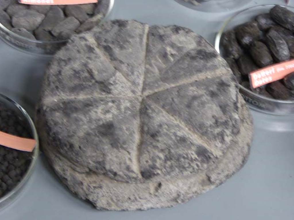 III.17, Herculaneum, September 2016. Carbonised bread, found in this location, now in deposits. Photo courtesy of Michael Binns.
According to Monteix, apart from dividing the upper area into six portions, the shape of the cut implies the use of a cord to model the dough during its rise. 
An unreadable seal has been applied to the upper surface.
See Monteix, N. 2010. Les lieux de métier. Boutiques et ateliers d’Herculanum. Ecole française de Rome, (p.153).
