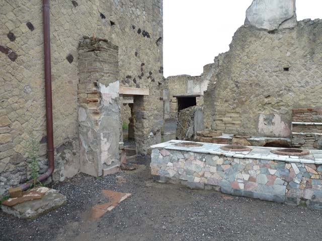 IV.16, Herculaneum, September 2015. Looking south-west across counter.
On the left, in the south-east corner, is a floor of tiles which has been interpreted as the presence of a trace of a latrine. According to Maiuri, there was a cooking stone in the south-east corner.

