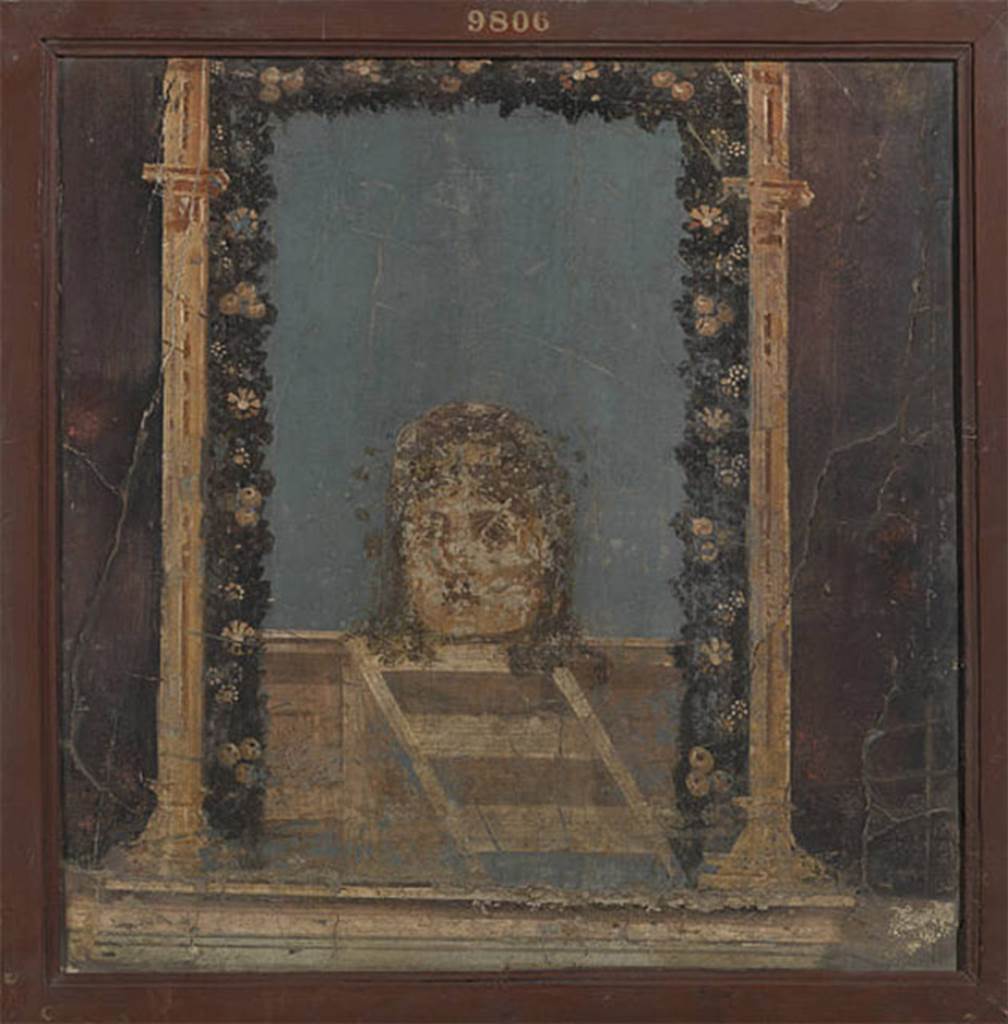 IV.21 Herculaneum. Triclinium 5, painting of Mask crowned with flowers on blue background, found at the west end (left side) of the north wall.
Detached from the wall 20th – 21st June 1749.  
Now in Naples Archaeological Museum. Inventory number 9806.