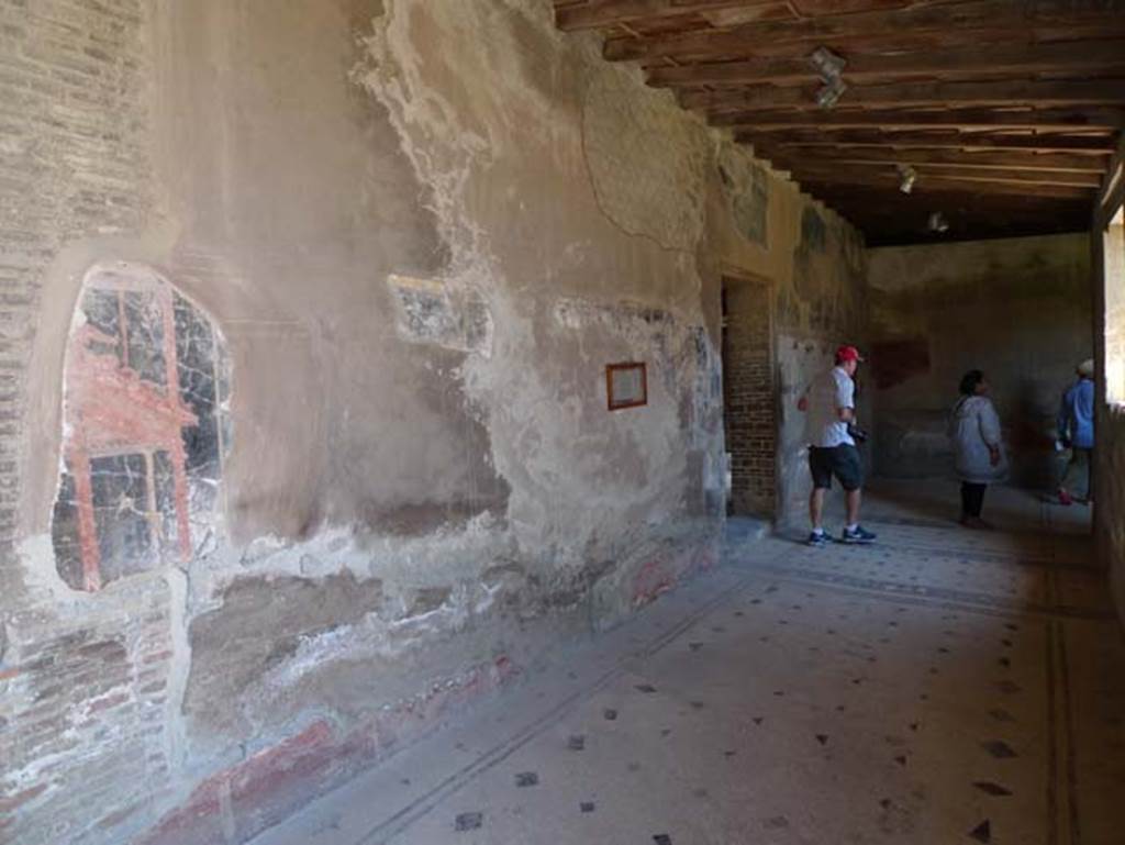 IV.21, Herculaneum, June 2017. 
Cryptoporticus 28, looking east along portico 28 towards doorway from room 24, the atrium, and towards Cryptoporticus 29.
Photo courtesy of Michael Binns.
Maiuri wrote that the ample quadriporticus (Cryptoporticus) having lost the architectonic element of the columns, now assumed the more convenient form of a corridor with windows, whilst it preserved the wall decorations and that of the flooring. The charming little pictures that still survive inserted into the panels on the walls, with scenes of Cupids Playing, belong to a longer series of pictures which were detached during the preceding excavations and are now preserved in the Naples Museum.
See Maiuri, Amedeo, (1977). Herculaneum. 7th English ed, of Guide books to the Museums Galleries and Monuments of Italy, No.53, (p.61-63).
According to Deiss, In front of the dining room and paralleling the long sides of the rectangle, runs a covered gallery without columns. The floor is black and white mosaic. Along the length of the corridor, panels show cupids at play, games like Blindmans bluff, and Hide and Seek. Most of the painted panels were removed to Naples Archaeological Museum.
See Deiss, J.J. (1968). Herculaneum, a city returns to the sun. London, The History Book Club, (p.41).

