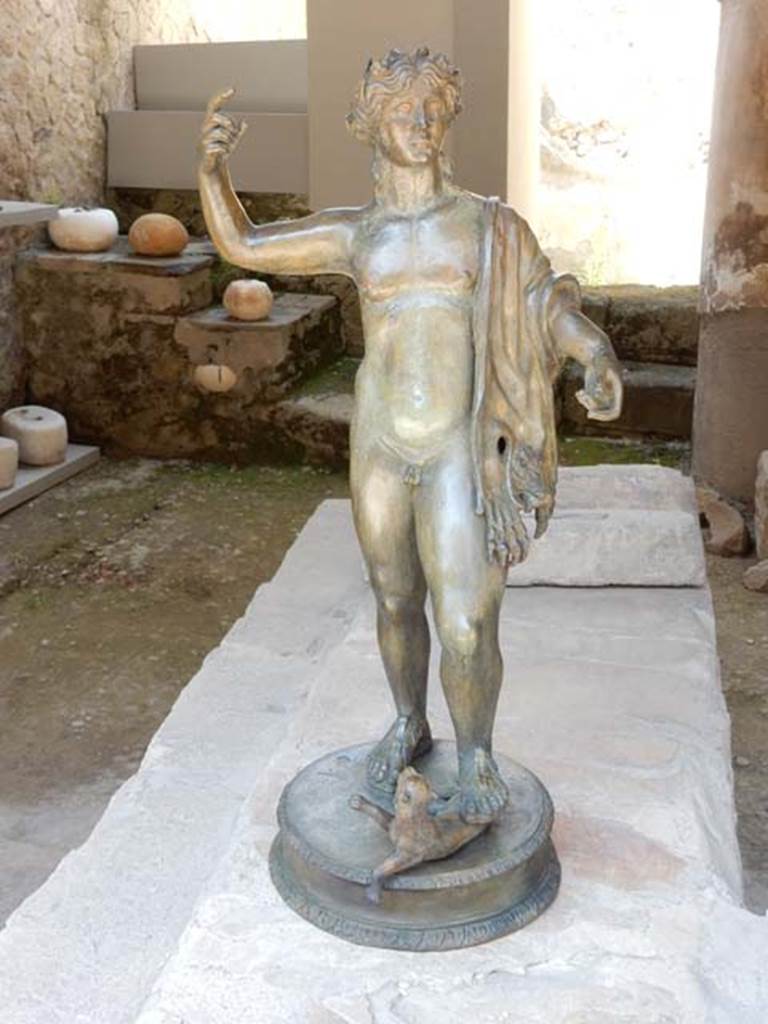 VI.12 Herculaneum. May 2018. 
Reproduction bronze statuette of Bacchus with decoration of gold, silver and copper, also awaiting repair in this metal worker’s workshop. 
On the counter behind the statue are two lead ingots, see Cooley below.
At the rear displayed on the steps are terracotta pots, and limestone weights. Photo courtesy of Buzz Ferebee. 
According to Cooley, “Two lead ingots from the Spanish peninsula were found. They bear official stamps relating to their production, export and weight, together with a numerical graffito comparing their actual weight with a standard weight.”
(ingot of 35kg.) Felix; Faustus; Adatrima?, Cu[-] Aug[-]; 8.
(ingot of 34kg.) Photiaca; C L(--) Hel(--); Ada[trima?] C C(-) H(-); 4.      (AE (2007) 415-16)
See Cooley, A. and M.G.L., 2014. Pompeii and Herculaneum: A Sourcebook. London: Routledge, (p.267, H81).

