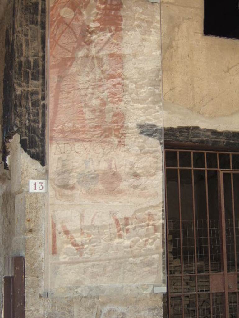 VI.13 Herculaneum on left, VI.14 on right. May 2006. 
Painted sign on pilaster between house entrance and shop. Looking south.
At the top is a painted figure. 
The shop sign showed four jugs of different colours, naming and pricing the drinks sold here together with the shop sign AD CVCVMAS (Ad Cucumas), written above the jugs.
The painted graffiti NOLA in red letters can also be seen on the lower part.
