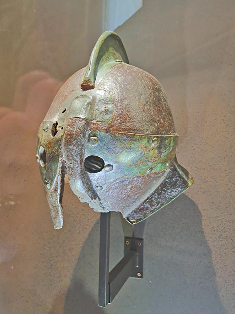 From Herculaneum. Roman iron gladiator helmet. Provenance unknown.
This helmet is of the type used by a Secutor gladiator.
Its rounded shape and small eye holes were designed to counter the net and trident of the Retiarius.
The Secutor was specially trained to fight a Retiarius, a type of lightly armoured gladiator armed with a trident and net.
The retiarius was thus faster and would try to tire the secutor whose heavy armour and the difficulty of breathing in the helmet meant that he had to win quickly.
May 2021. On display in Naples Archaeological Museum. Photo courtesy of Giuseppe Ciaramella.

