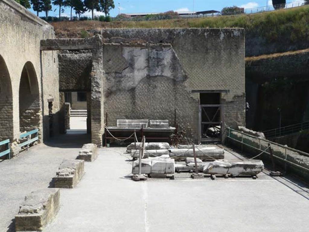 Herculaneum, September 2015. Sacred Area terrace, looking east towards doorway to large room 7 which contained a large podium against the north wall and masonry benches against the west and east walls. The remains of many columns and pilasters can be seen laid on the terrace floor.  Originally this was a large rectangular garden area in which two labra were found.
See Camardo, D, and Notomista, M, eds. (2017). Ercolano: 1927-1961. L’impresa archeologico di Amedeo Maiuri e l’esperimento della citta museo. Rome, L’Erma di Bretschneider, (p.284, Scheda 59).

