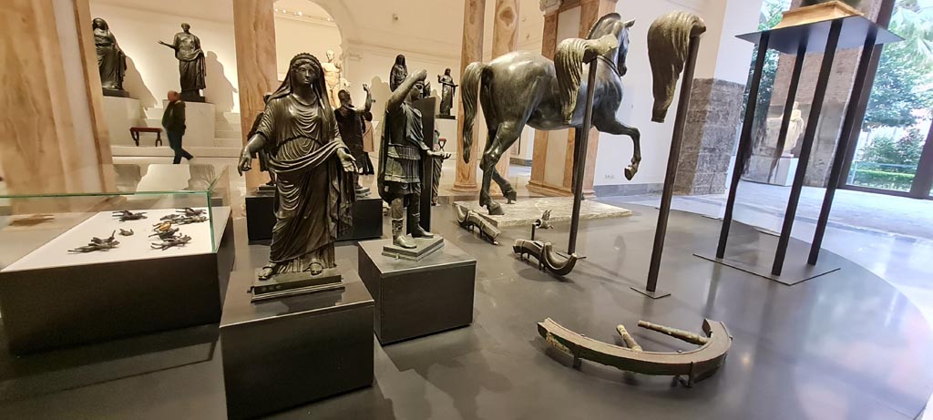 Herculaneum, April 2023. Bronzes in “Campania Romana” gallery in Naples Archaeological Museum. 
On the left in the glass case are the small bronze chariot attachments, centre are the bronzes statuettes from the parapet of the quadriga .
Exhibits in “Campania Romana” gallery in Naples Archaeological Museum. Photo courtesy of Giuseppe Ciaramella.

