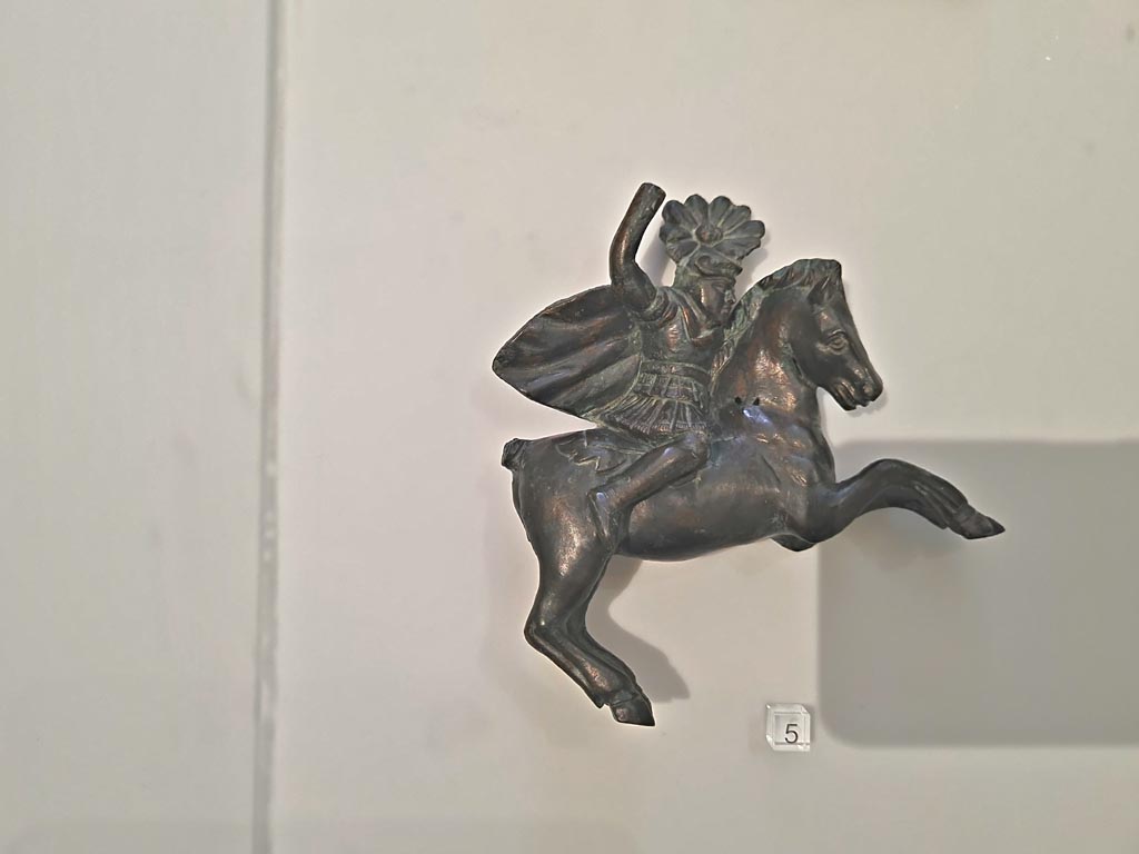Herculaneum, April 2023. Bronzes in “Campania Romana” gallery in Naples Archaeological Museum. 
Detail of bronze figure in glass case - small bronze chariot attachment in the form of a horseman. Photo courtesy of Giuseppe Ciaramella.


