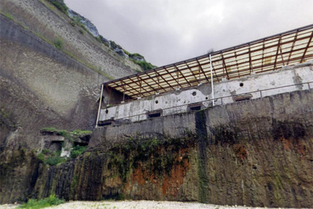 Villa dei Papiri, Herculaneum. 2004. The levels of the villa with the atrium level roof at the top.
According to Guidobaldi and Esposito, on the basis of the structures unearthed so far, the Villa seems to have been much more complex and monumental than previously envisaged, with at least two floors, whose residential use is demonstrated, and a third one for which use as a residential area is probable but not attested.
The first lower level has a façade covered in smooth white plaster and is marked by large quadrangular windows.
Four of these windows also have splayed oculi above and there is a series of at least six rooms (I-VI) on this level.
During the 1996-8 excavation, a second lower level bow windowed structure, protruding in respect to the front of the basis villae, was discovered at the west end of the façade. 
There is then a grand pavilion with a large rectangular swimming pool that led directly to the beach through a small staircase that faded into and mingled with the natural rock.
See Esposito D. and Guidobaldi M., 2010. New Archaeological Research at the Villa of the Papyri, in the Villa of the Papyri at Herculaneum. Berlin: De Gruyter, p. 23,; pp. 33ff, fig. 23; p. 41-2, fig. 32, notes 62-3. 


